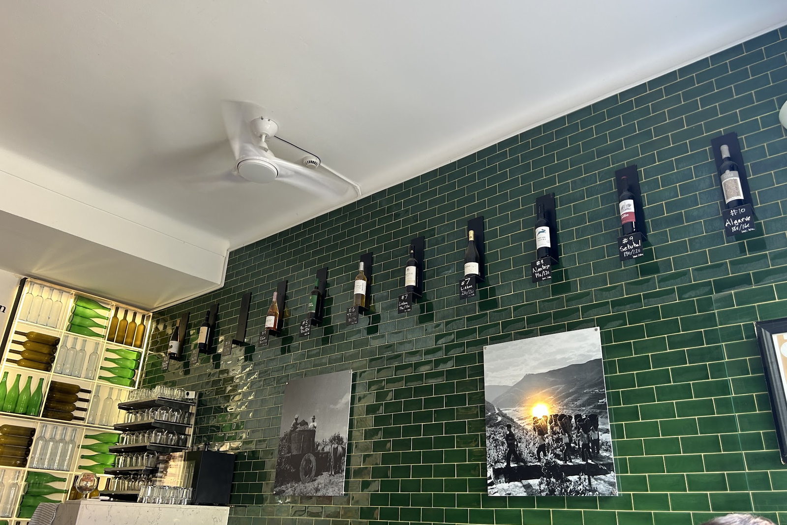 A sala do bar, com parede de azulejo verde e garrafas expostas